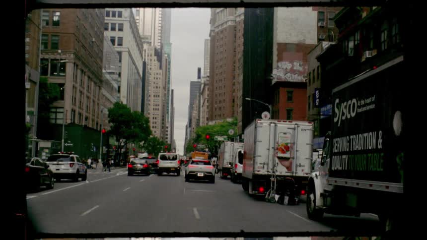 A busy city street scene is captured showing heavy traffic and towering buildings with a large sysco truck on the right