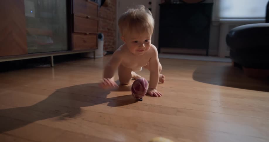 Little boy crawls across the floor knocking his toys across the room