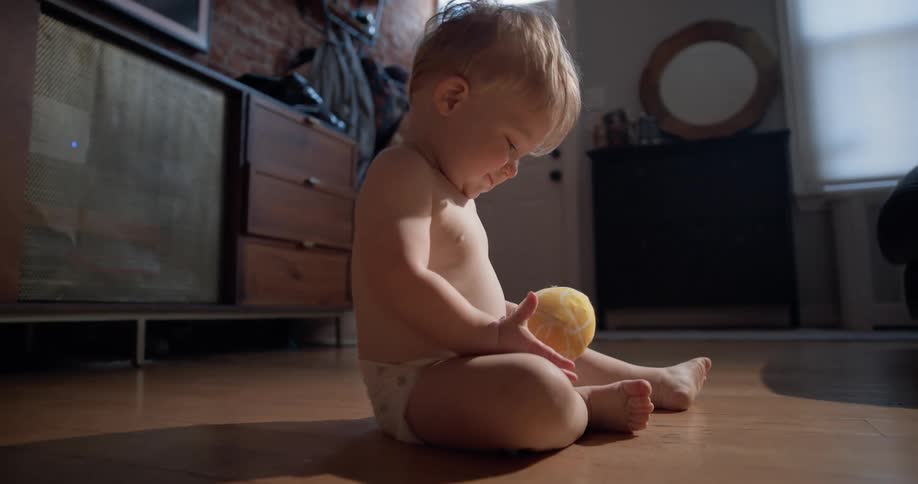 Baby holding a small ball while sitting on the floor of an indoor space