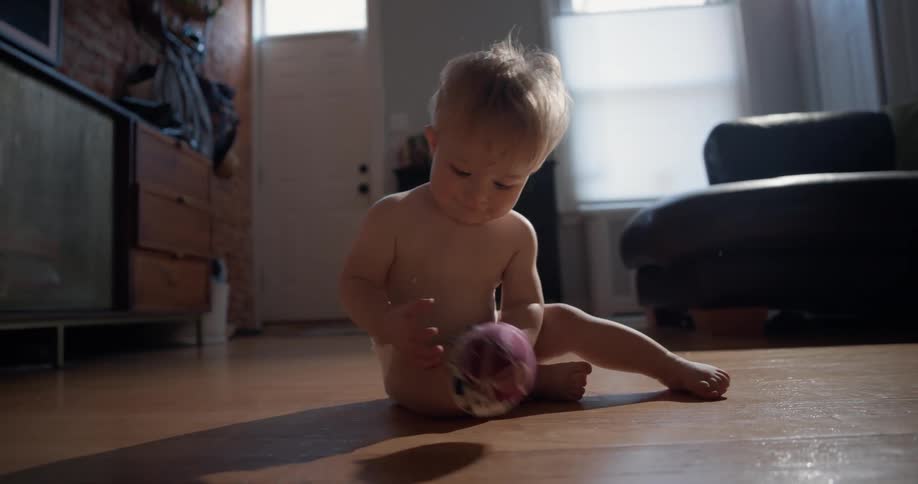 Baby reaching for a small ball while supported on the floor of an indoor space