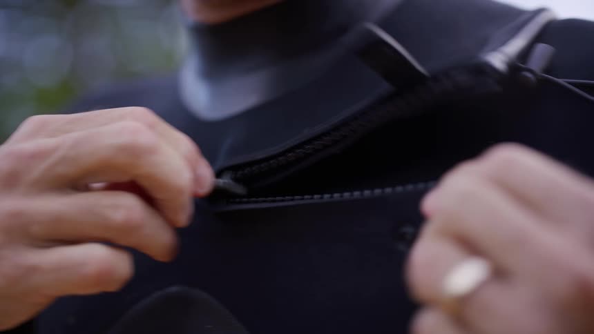 Male hands unzippinga part of a wet suit outdoors during day time