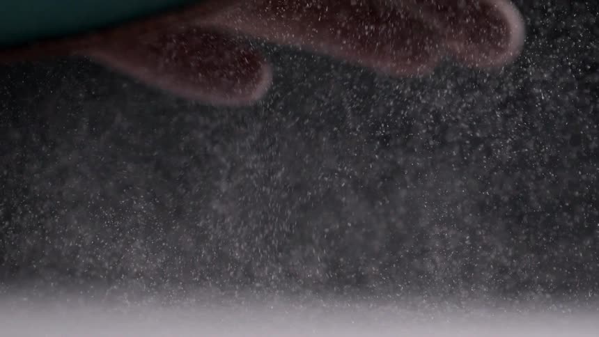 Fingers releasing dust particles above a white surface