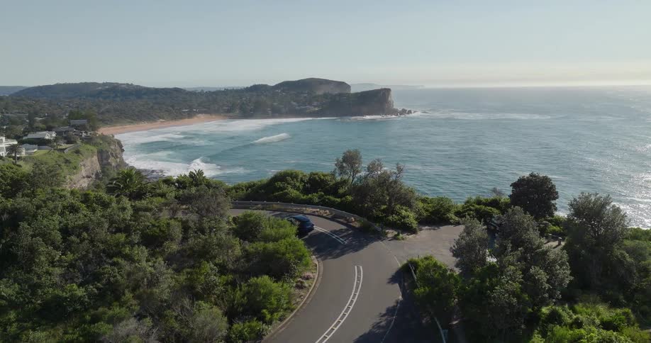 Curved road surrounded by vegetation with a view of a cove and cliffs in the background