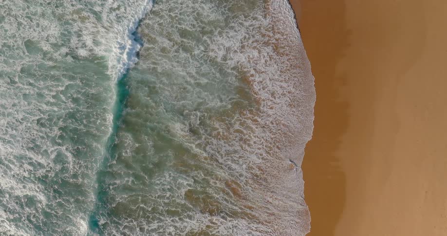 Aerial view of waves rolling in to shore and over sand on the beach