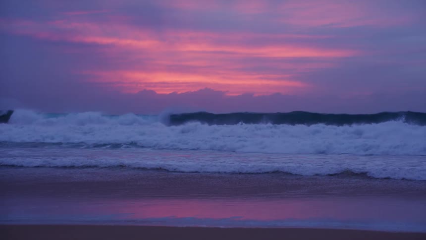 Strong waves breaking on the beach under a pink dawn sky