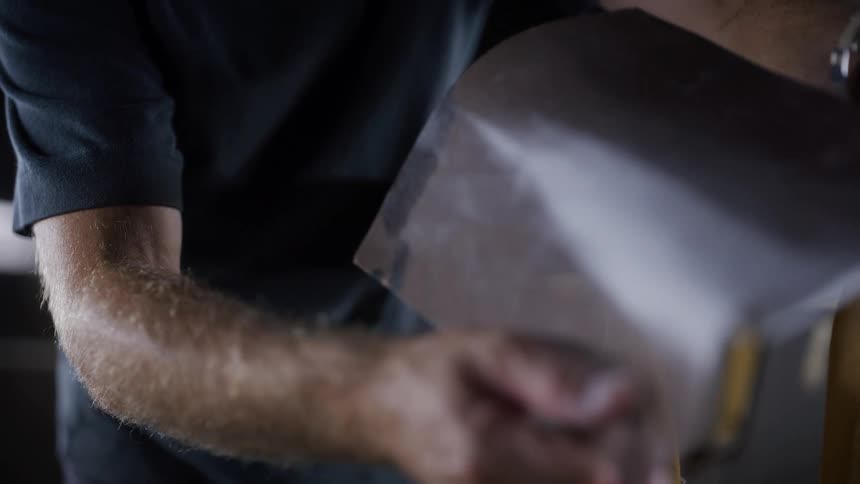 Male hands filing a surfboard on a stand indoors