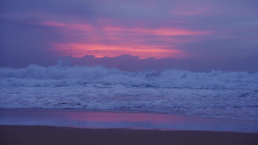 Waves breaking on the beach under a pink dawn sky