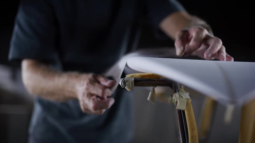 Man sanding the edge of a board supported on a padded stand