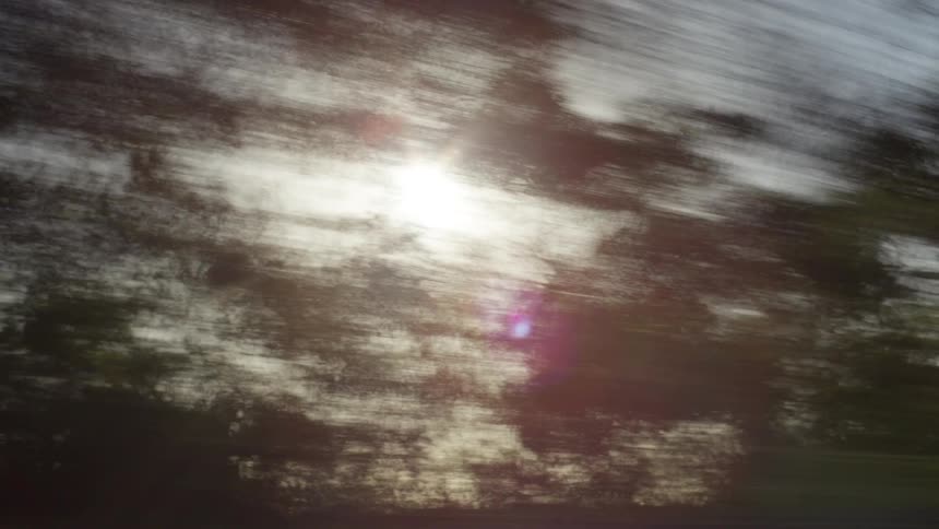 Sun behind blurred trees passing quickly outside a moving window