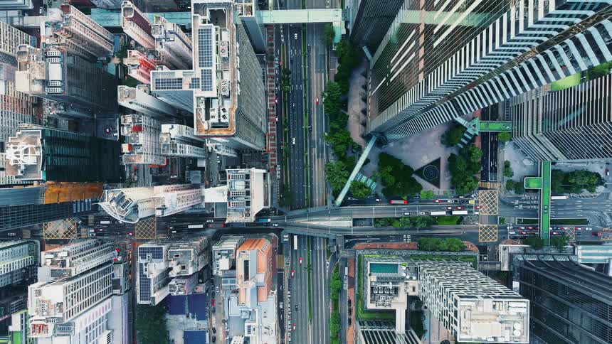 A top down aerial shot shows a dense vertical cityscape with skyscrapers busy streets with passing traffic and pedestrian overpasses