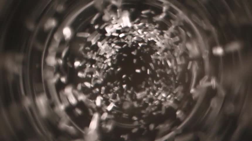 Metal grains swirl in a spiral motion inside a container viewed from above