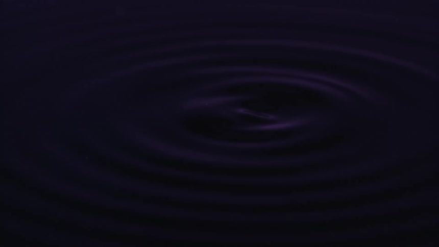 Concentric ripples spread across a dark still body of water or liquidthat turn into purple lit large splashing drops