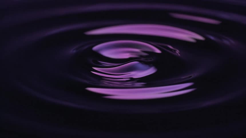 A dark liquid surface dramatically lit with purple light captures a highspeed closeup view of a droplet creating perfect expanding ripples and culminating in a tall complex splash column