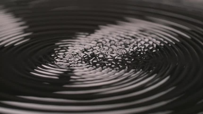 Smooth ripples on a dark liquid surface vibrate and transform into a complex textured pattern