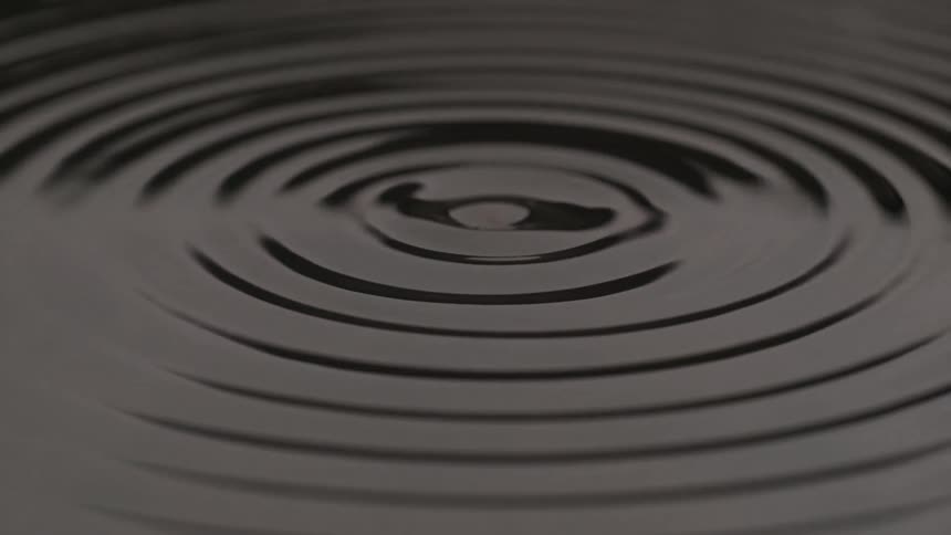 Dark liquid surface with a droplet lifted after impact