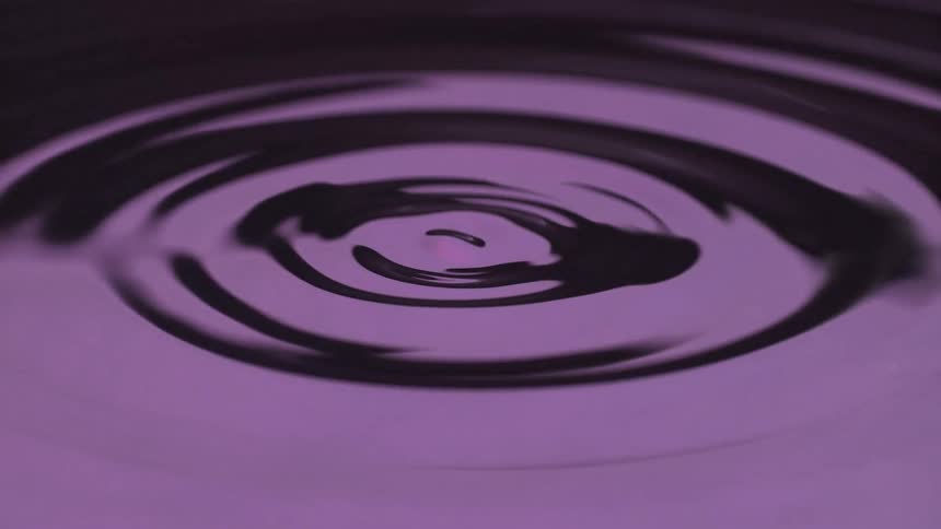 A close up of a purple liquid that begins with circular ripples before changing into large splashing dropletsto