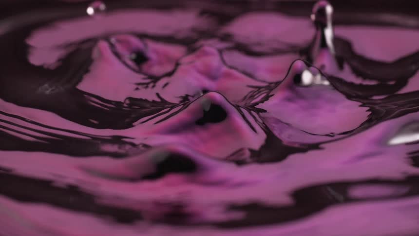 A purple liquid begins with ripples in a circular motion and slowly turns into drops forming and splashing then bubbling