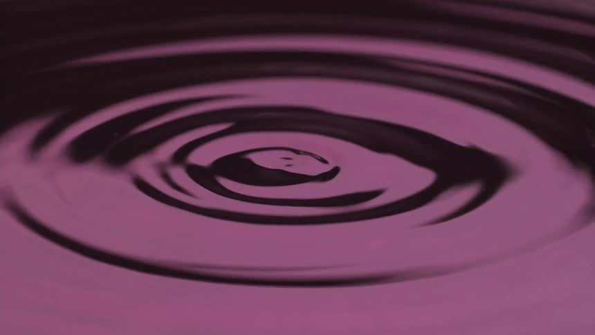 Ripples on a purple liquid surface erupt into a chaotic splash