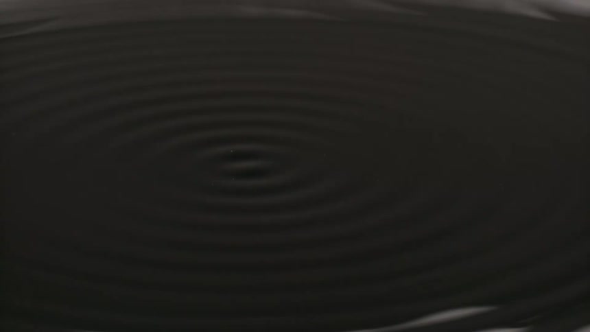 A black liquid ripples in a circular motion a substance that looks like snow falls onto the liquid