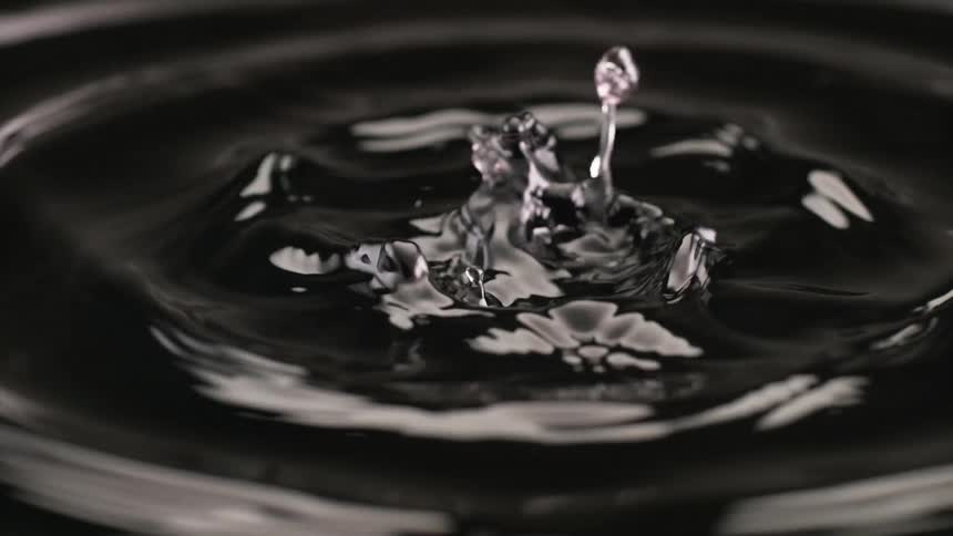 A black liquid starts out rippling in a circular motion before turning into large drops splashing then bubbling
