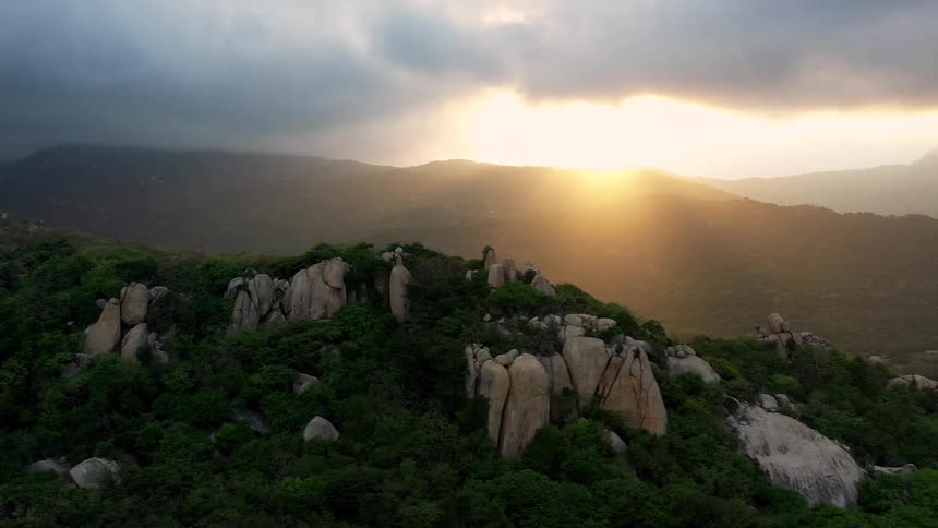 Green hills with large scattered rocks and a beam of sunlight passing through dense clouds