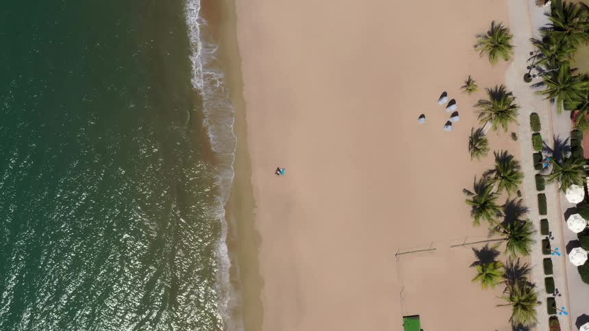 Beach seen from above with a wide sand strip waves near the shore and a few structures scattered in the background