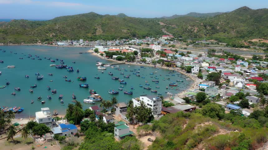 Rural city on the coast surrounded by hills next to a beach with many boats on the sea outdoors during day time