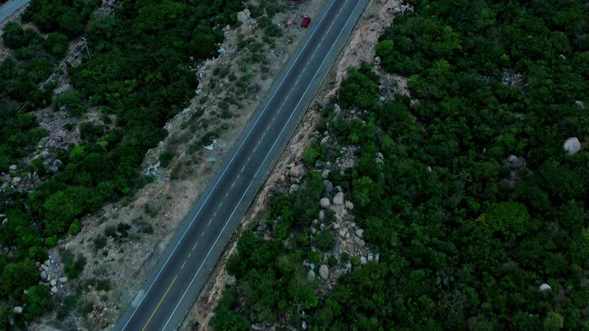 Paved winding road between rocky areas and dense vegetation with two cars driving