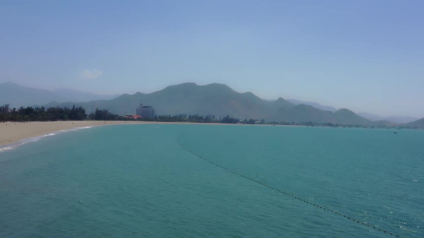 Long beach beside calm sea with a mountain range in the background