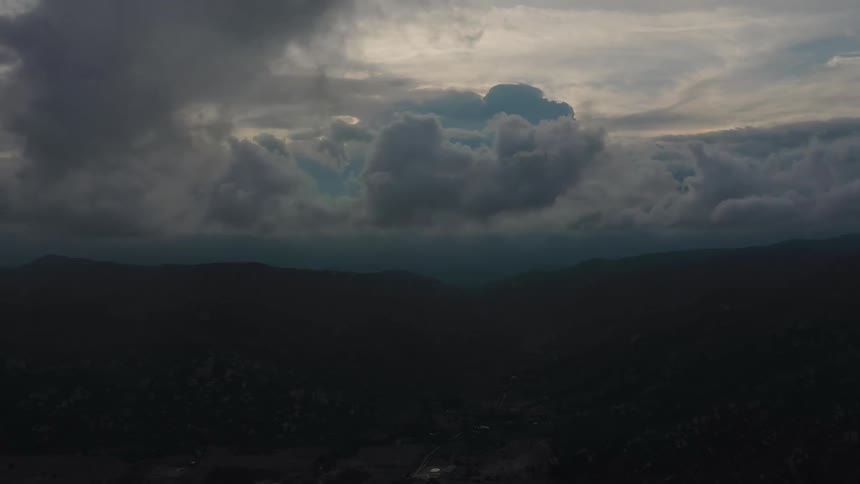 A cloudy evening settles over the mountain range with thick clouds drifting across the sky and covering the setting sun casting a soft muted glow over the peaks