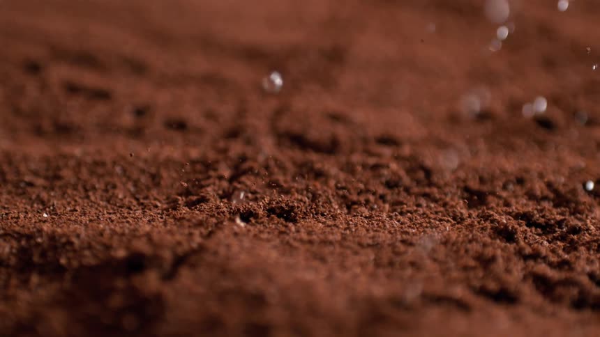 A closeup lowangle shot captures individual slowmoving water droplets falling and briefly bouncing off a dark brown textured surface