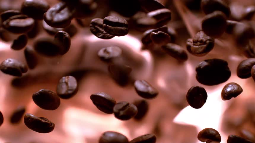 Dark coffee beans suspended against a bright background