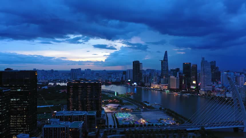 A city skyline stretches across the horizon at evening with a long bridge linking two cities dark clouds loom overhead covering the sky