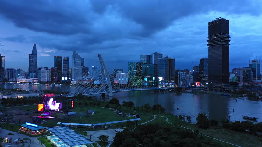 A city skyline stretches across the horizon at evening with a long bridge linking two cities dark clouds loom overhead covering the sky
