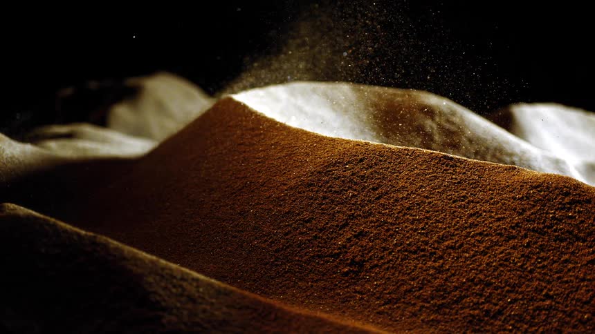 Mounds of brown powder with particles dispersing above the lit surface