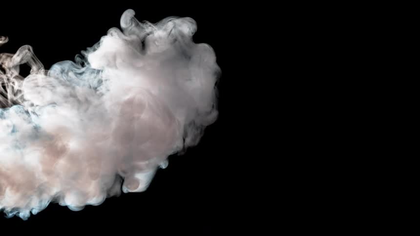 Dense white opaque smoke slowly billows and expands across the lower left corner of the frame against a completely black background showcasing the curling and wispy movement of the vapor