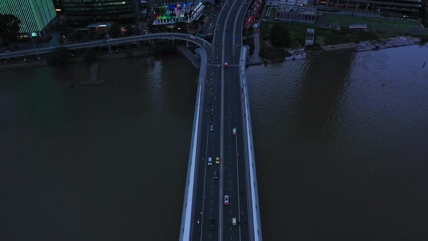 Cars stream across a link bridge at sunrise merging into the busy city highway as the first light of day paints the skyline in warm hues