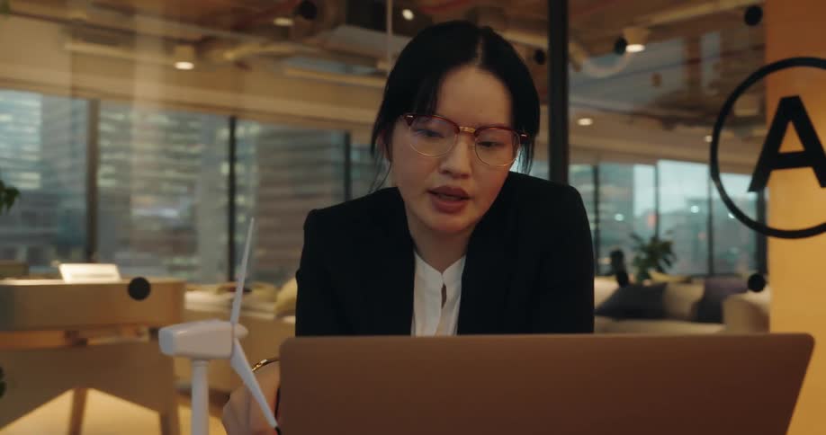 Woman talking as she works on a laptop computer with a model of a wind turbine on the desk