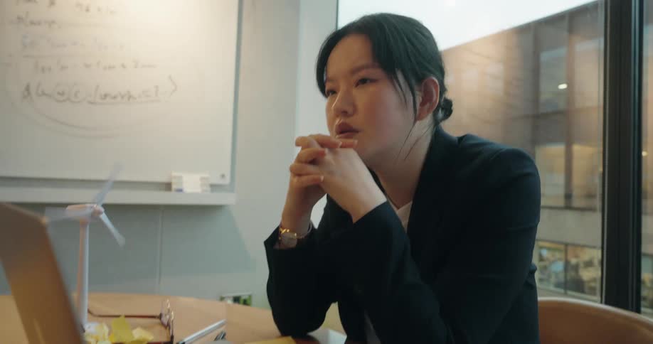 Woman seated at a table looks at a laptop beside a small wind turbine model