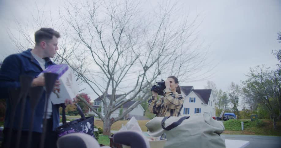 The man poses for the camcorder while holding items from a yard sale