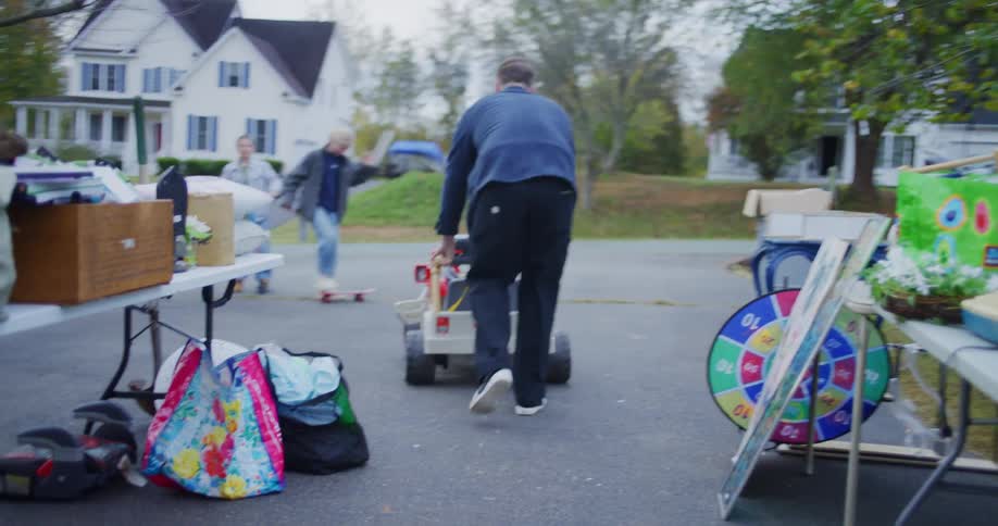 Man pushes a childs electric toy car while children watch in the driveway