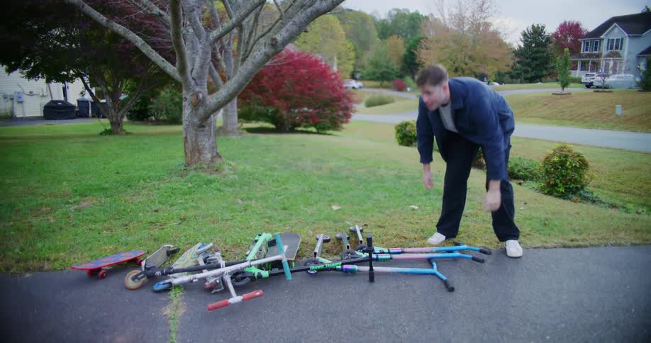 Man arranges scooters and skateboards scattered on the driveway