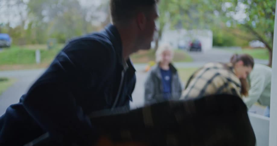 Several people are standing on a house driveway moving several items including a blanket and table