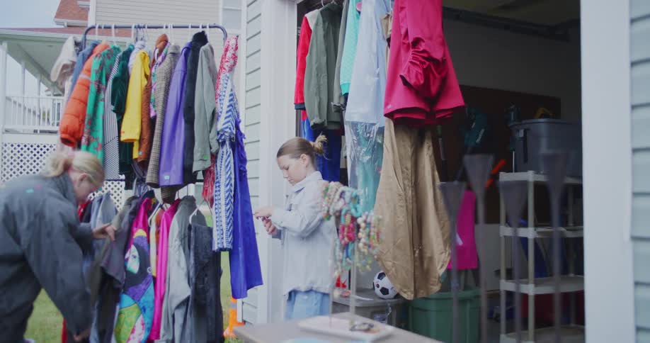 Children look at clothes hanging on a rack set up in the garage