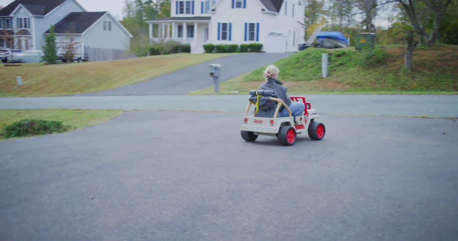 Child drives a toy electric car while another stands beside watching