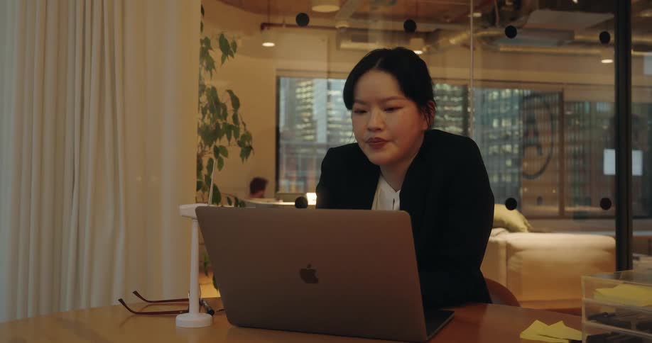 Woman walks into the office and sits at her desk as she opens her laptop computer and types