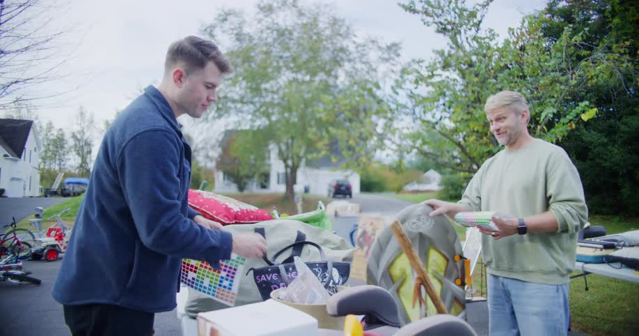 Men organize items and stickers on a table at a garage sale