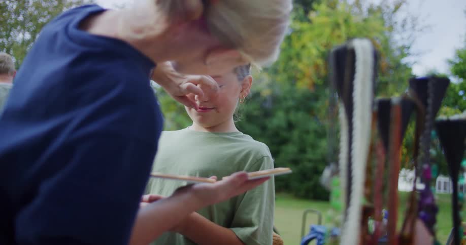 Child covers their eyes while another person holds a paint palette in front