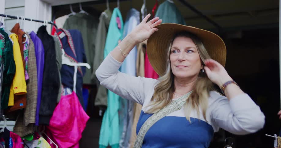 The woman smiles while trying on a hat at a yard sale