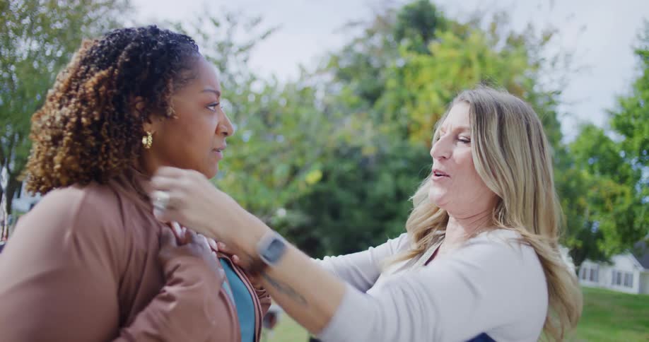 Woman adjusts a necklace on another person at an outdoor garage sale